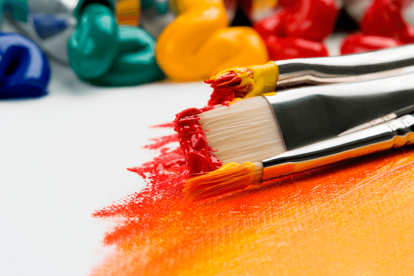 Paint-loaded brushes drawing red and orange pigment across a white surface